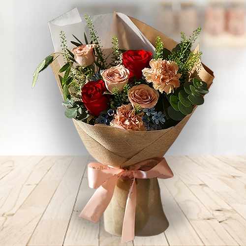 A Charming Bouquet Of Red And Cappuccino Roses, Caramel Carnations, And Blue Oxypetalum, Elegantly Wrapped For Delivery Across Singapore.